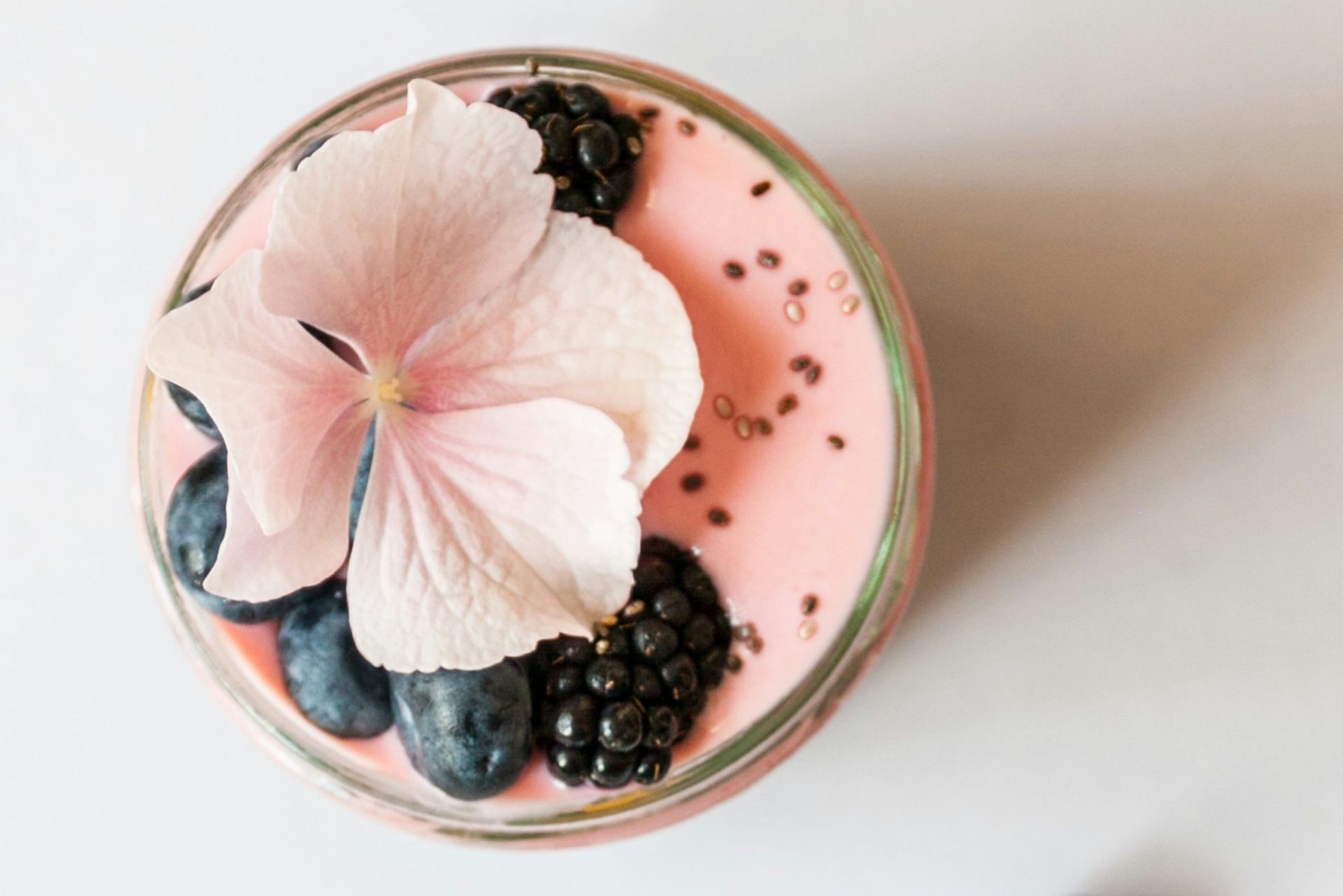 pink beverage on glass with blackberries and pink flower on top